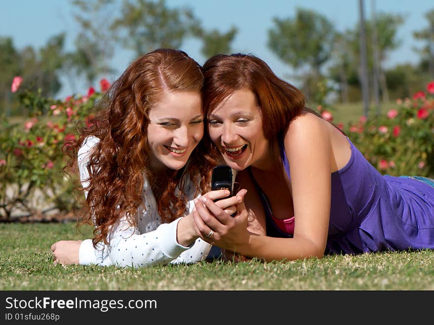 Two Girlfriends With A Mobile Phone In Park