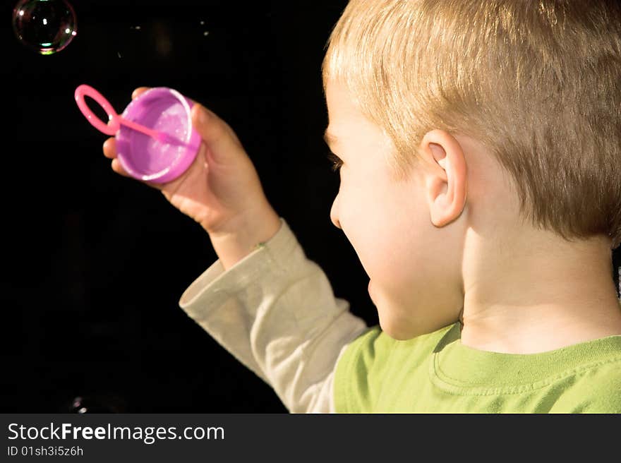 Young boy blowing bubbles outside in the sun