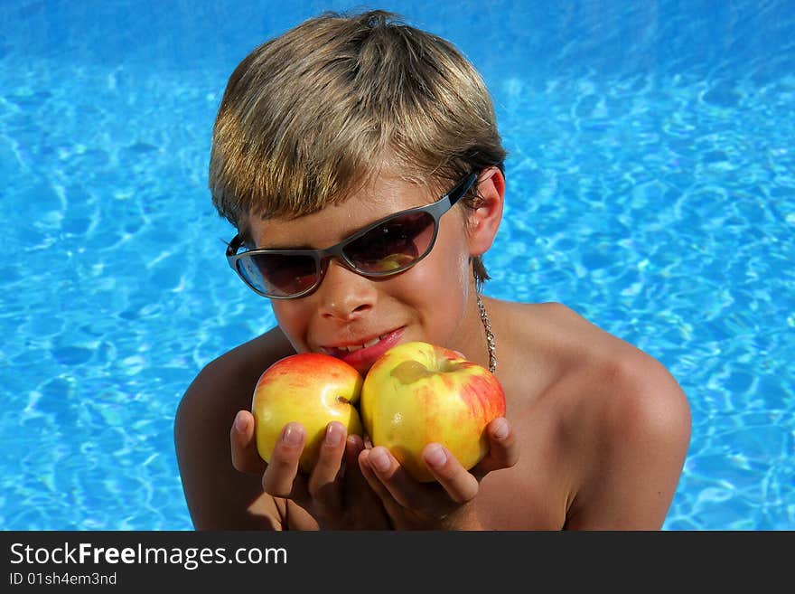 A 10 year old smiling American - German boy with sun glasses sitting at a swimming pool and presenting delicious apples in the summer sun . A 10 year old smiling American - German boy with sun glasses sitting at a swimming pool and presenting delicious apples in the summer sun