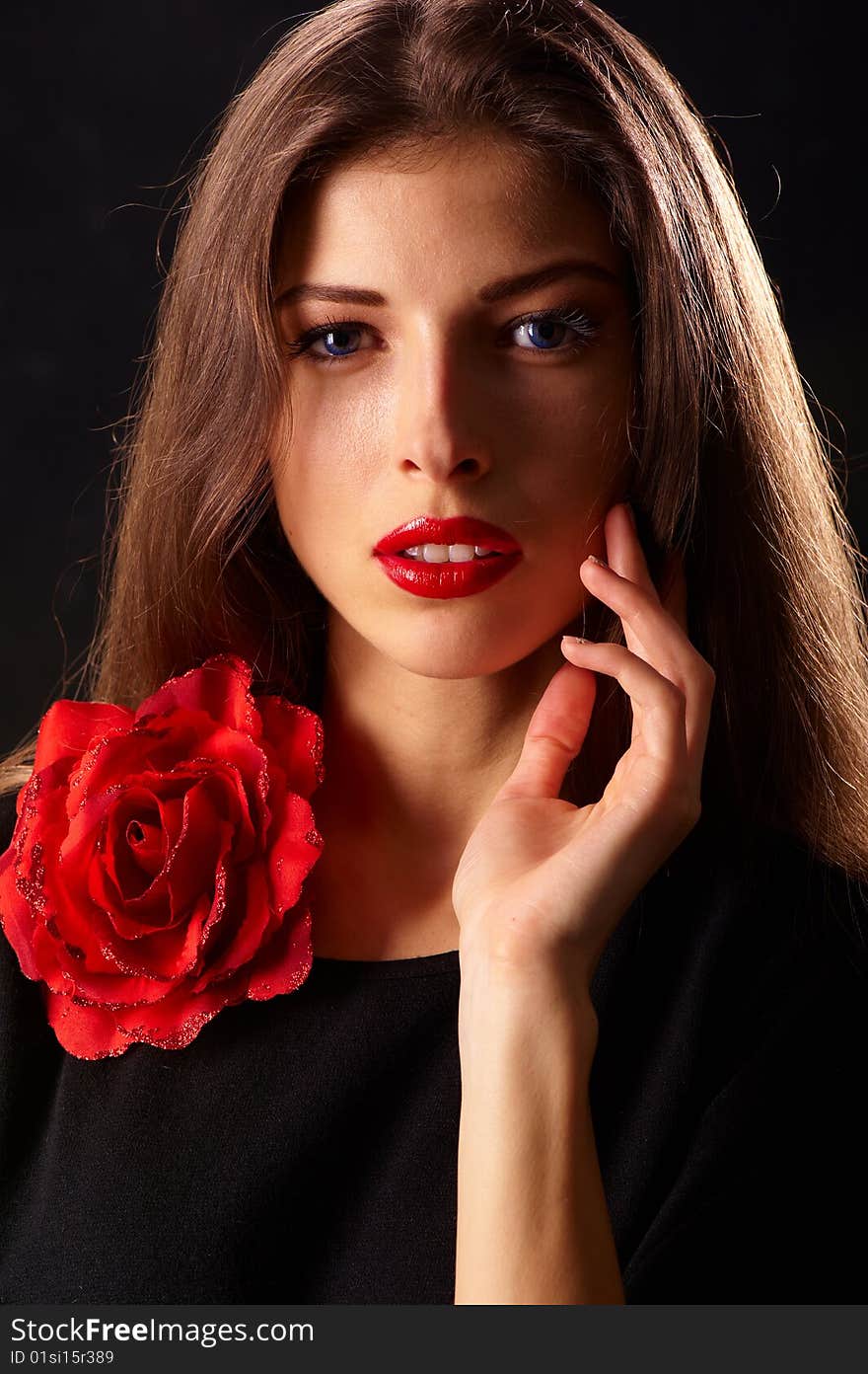 Portrait of a young beautiful brunettes with red lips in a black blouse decorated with a rose. Portrait of a young beautiful brunettes with red lips in a black blouse decorated with a rose