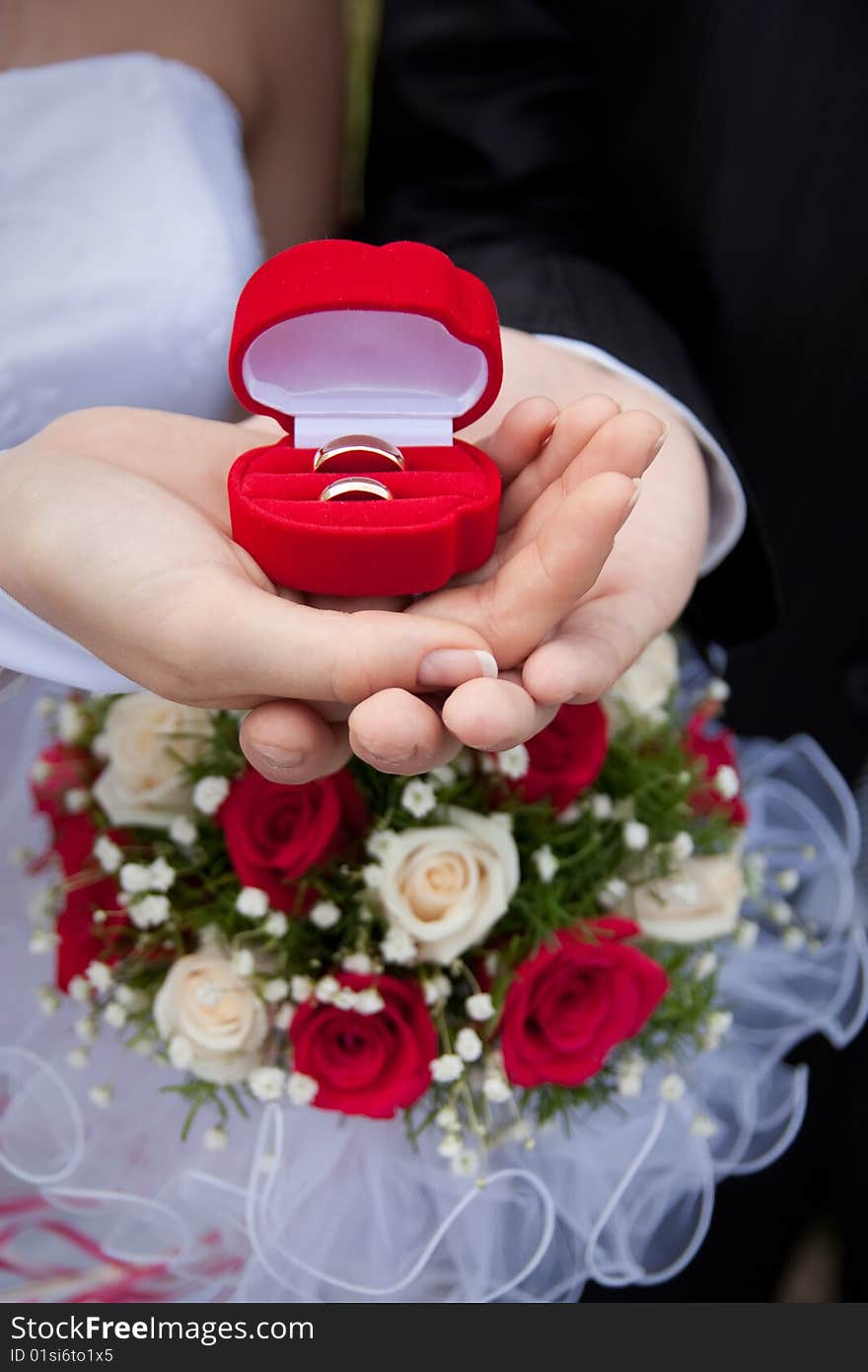 Wedding rings in hands of a newly-married couple on a background of a bouquet