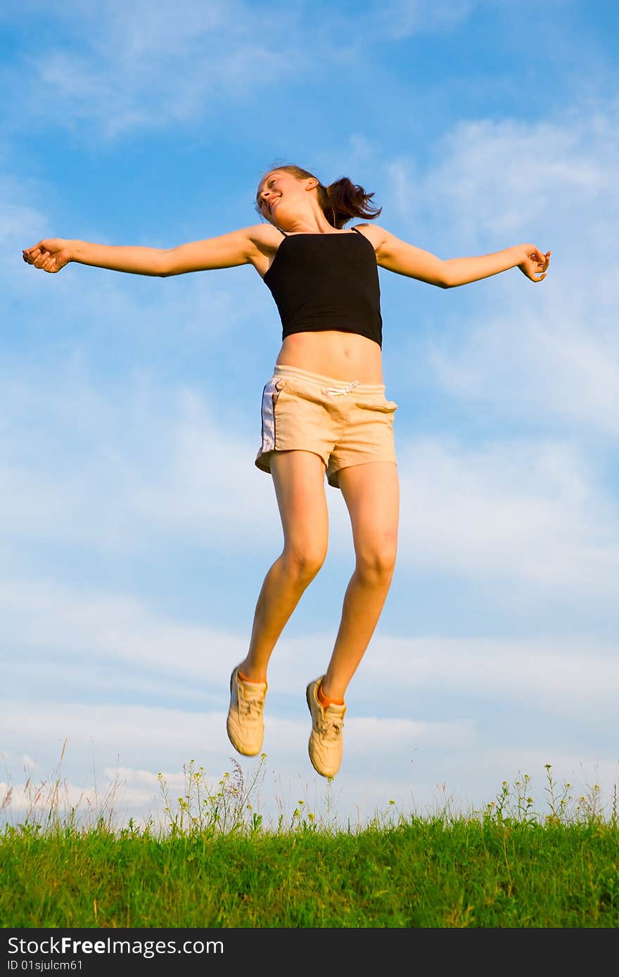 Happy young woman is jumping on green grass under sky