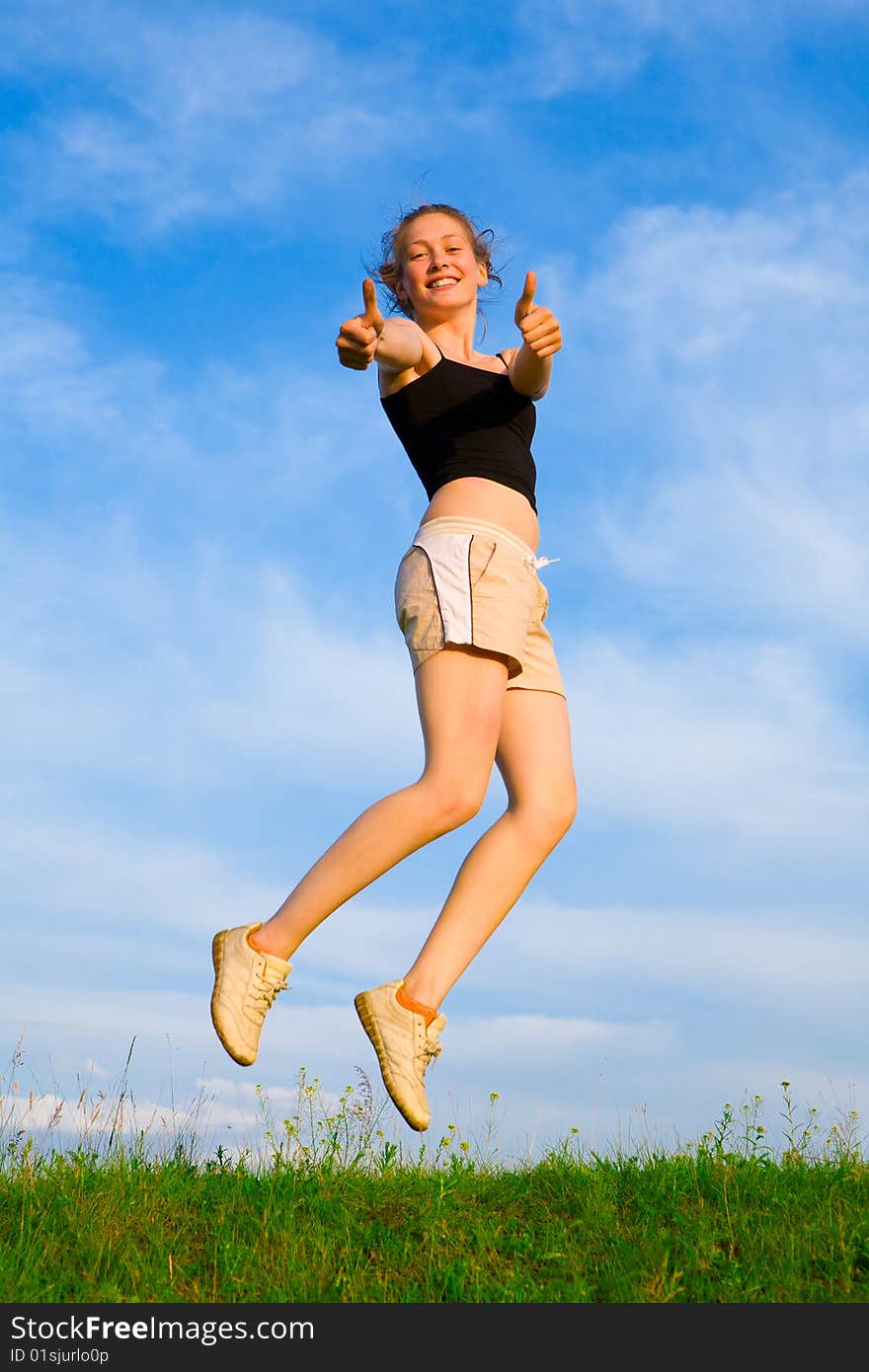 Happy young woman is jumping on green grass under sky