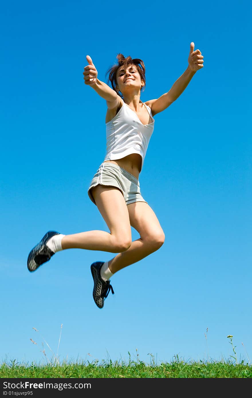 Happy young woman is jumping on green grass under sky