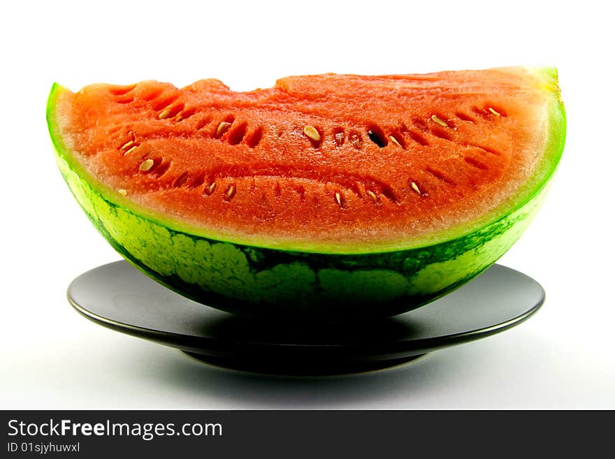 Slice of watermelon with green skin and red melon with seeds on a black plate with a white background. Slice of watermelon with green skin and red melon with seeds on a black plate with a white background