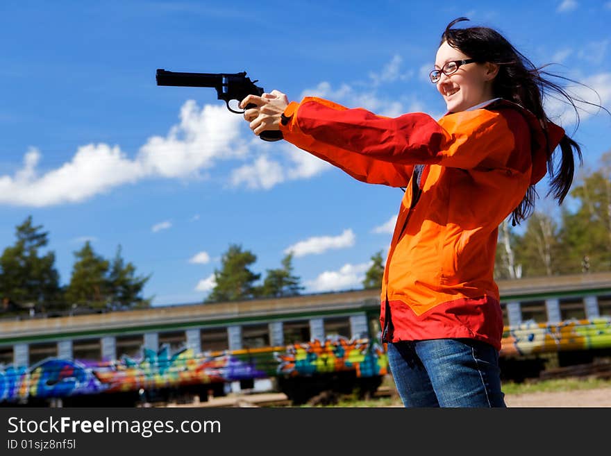 Young woman with long black hair holds a pistol and aims. Railway station. Young woman with long black hair holds a pistol and aims. Railway station.