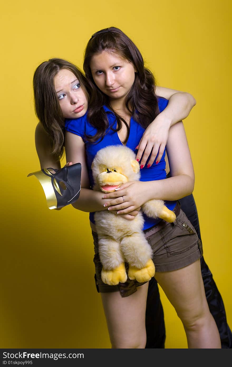 Two beautiful smiling friends girls with yellow toy-monkey isolated on yellow background. Two beautiful smiling friends girls with yellow toy-monkey isolated on yellow background.