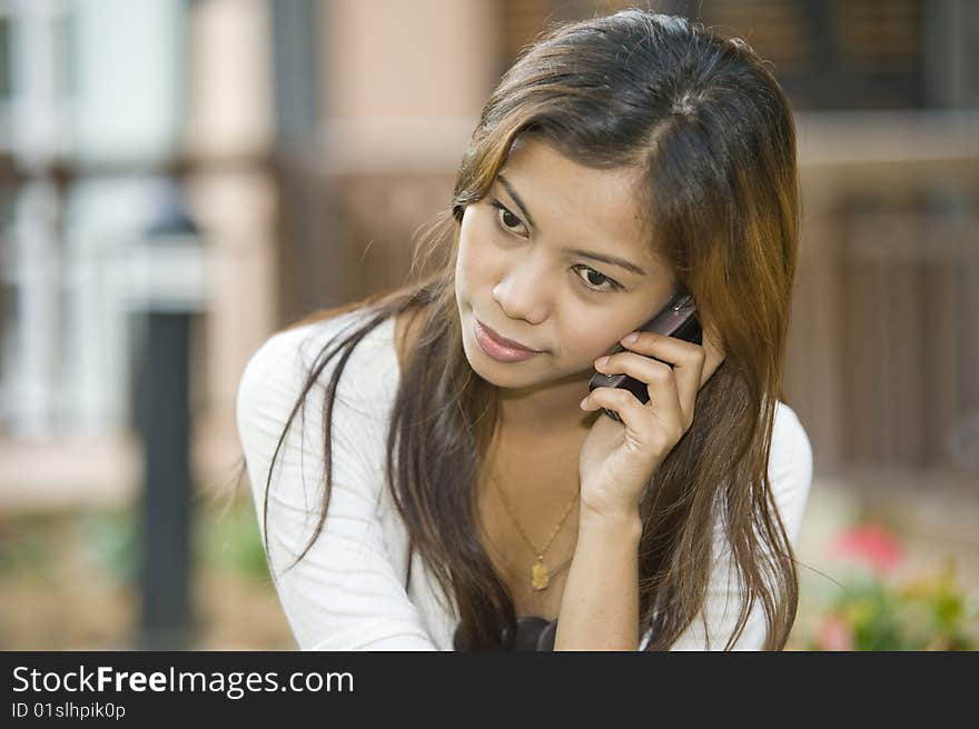 An asian girl is busy talking on the phone with a friend.