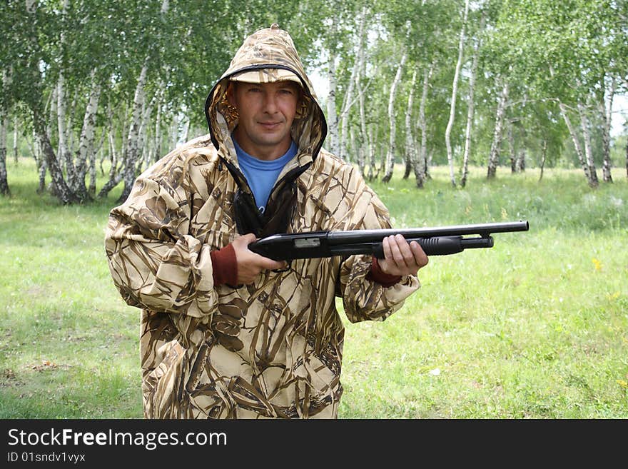 Person in the protectiving suit with a gun on a background of a wood. Person in the protectiving suit with a gun on a background of a wood