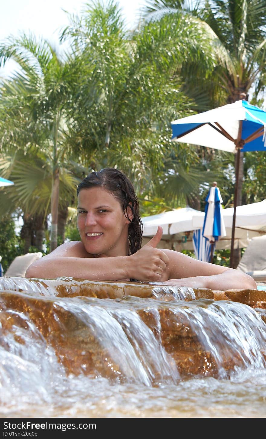 Young woman in a beautiful pool with palms in the background. She is showing a thumbs up sign. Young woman in a beautiful pool with palms in the background. She is showing a thumbs up sign.