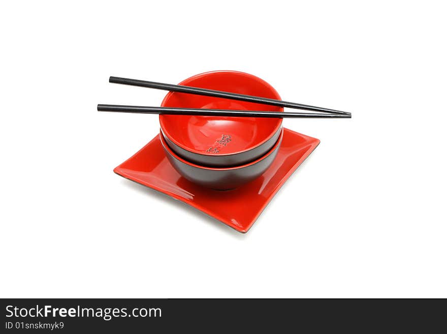 Black chopsticks on two red and black Japanese bowls and square plate isolated. Black chopsticks on two red and black Japanese bowls and square plate isolated