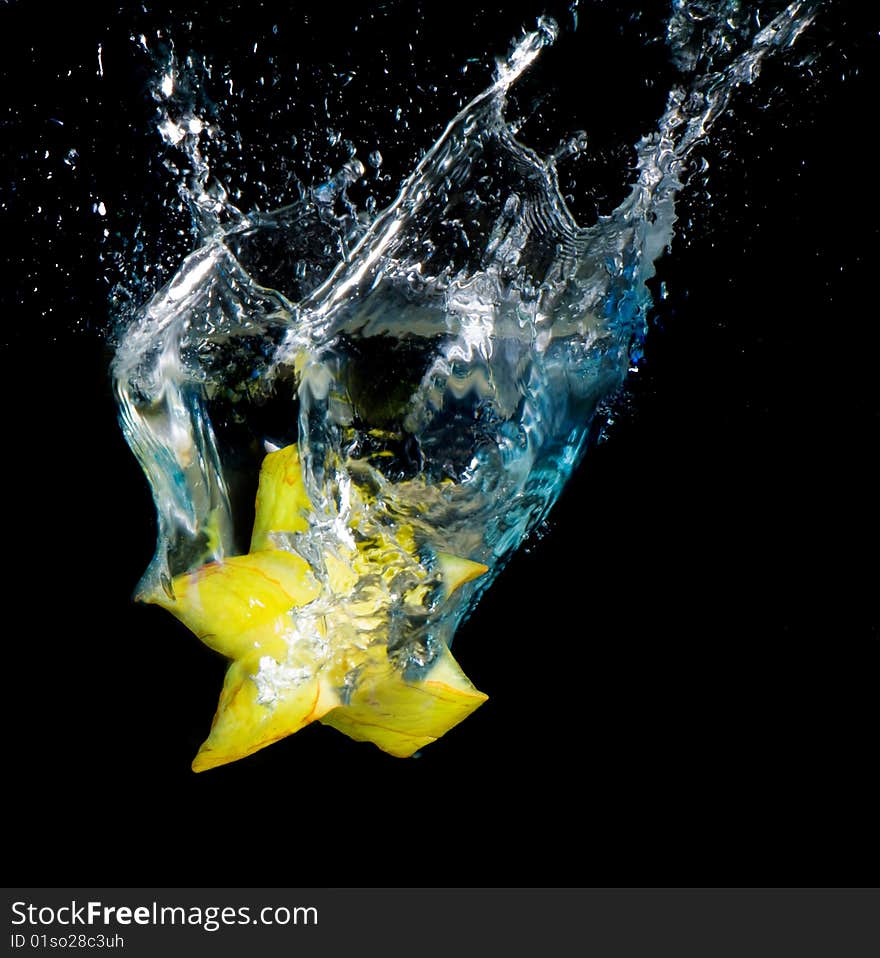 Starfruit tumbled into water, a lot of sparks and drops on black background, isolated