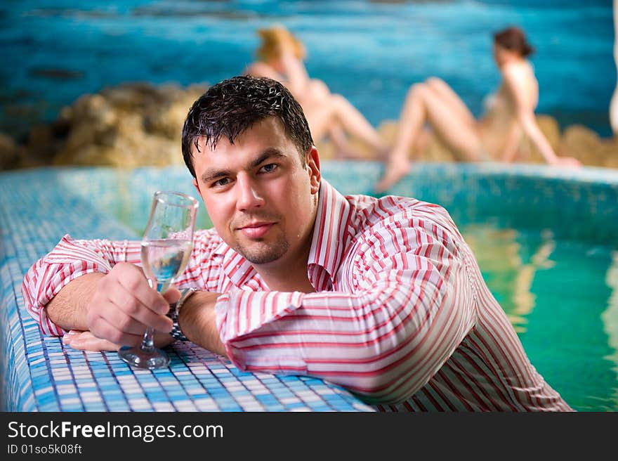 Portrait of a young man with a glass in the pool against the backdrop of two beautiful girls. Portrait of a young man with a glass in the pool against the backdrop of two beautiful girls