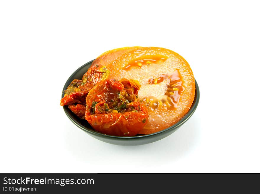 Sun dried tomatoes and slices of tomatoes in a small black bowl on a white background. Sun dried tomatoes and slices of tomatoes in a small black bowl on a white background