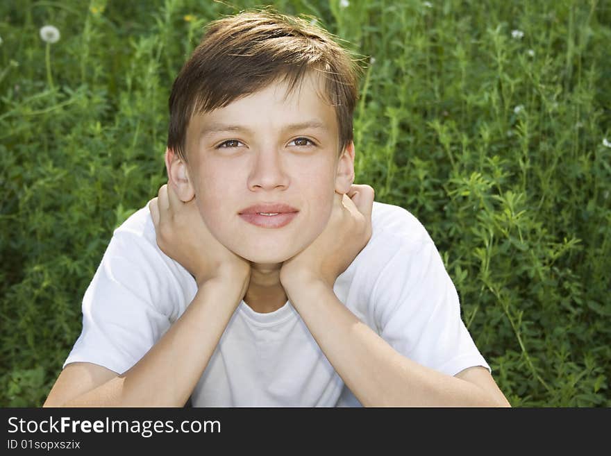 Dreamy teenager is relaxing, and he sit on the grass. Dreamy teenager is relaxing, and he sit on the grass