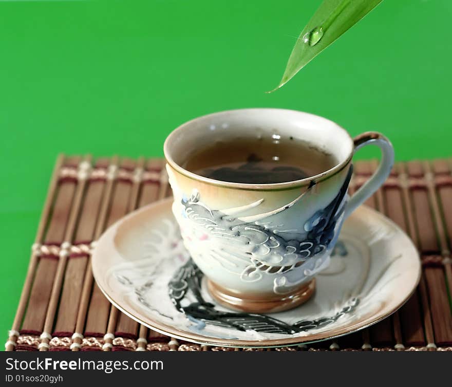 A cup of green tea and a drop of water on a green background