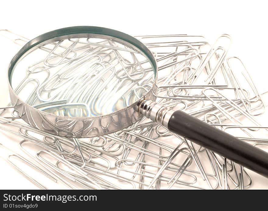 Magnifying glass on top of a stack of paperclips against a white background