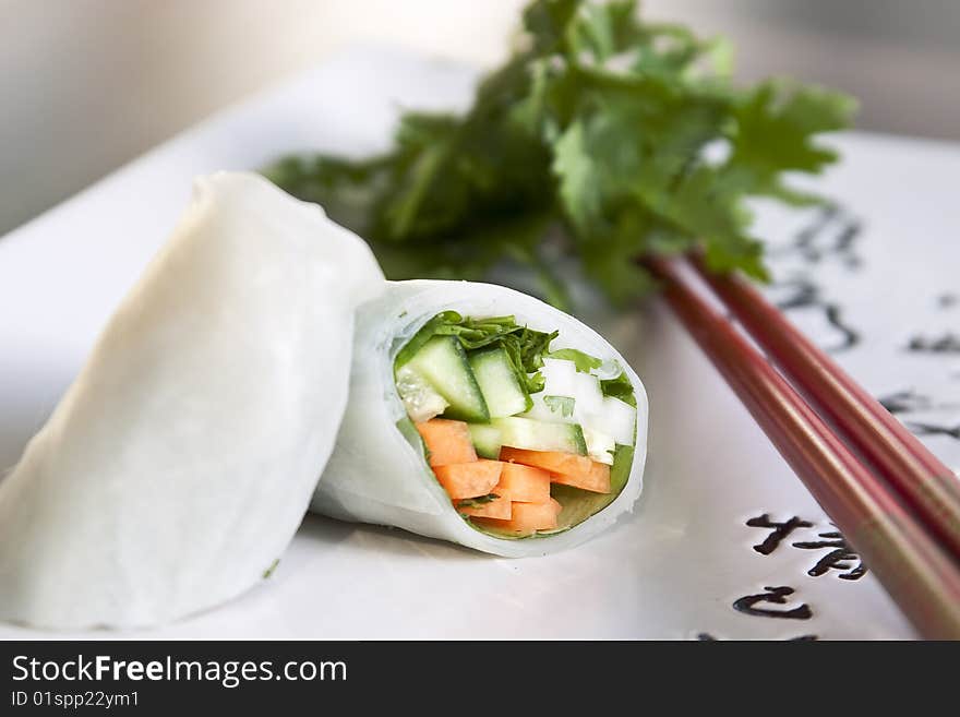 Springroll on a plate with chop sticks with greens in the background. Springroll on a plate with chop sticks with greens in the background