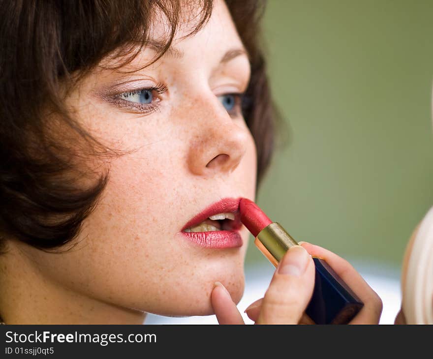 Brown-haired girl makes a make-up. Looks aside. Green background. Lipstick red. Lipstick. Eyes blue. Low depth of field. Brown-haired girl makes a make-up. Looks aside. Green background. Lipstick red. Lipstick. Eyes blue. Low depth of field.