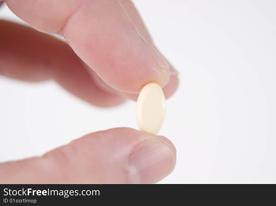 Two fingers holding a single cream prescription pill. Two fingers holding a single cream prescription pill