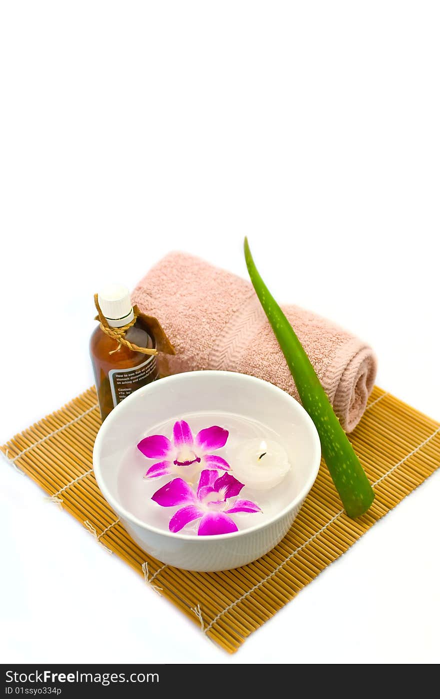 A white porcelain bowl with a tealight candle and two purple orchids floating in water, an aloe vera needle, a rolled up hand towel and a bottle of aromatherapy oil on a bamboo mat make up an assortment of items that are used in spas. A white porcelain bowl with a tealight candle and two purple orchids floating in water, an aloe vera needle, a rolled up hand towel and a bottle of aromatherapy oil on a bamboo mat make up an assortment of items that are used in spas.