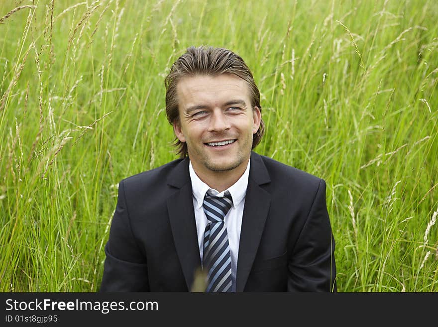 Smiling young businessman is sitting in a field