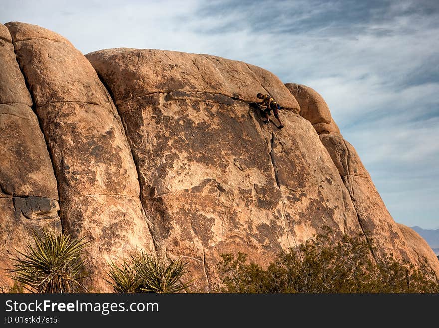 A rock climber making it to the top of a large rock at Joshua Tree National Park. A rock climber making it to the top of a large rock at Joshua Tree National Park.