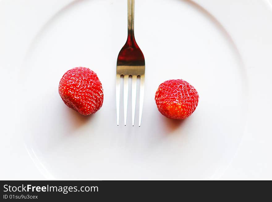 Fork among strawberry on the white plate