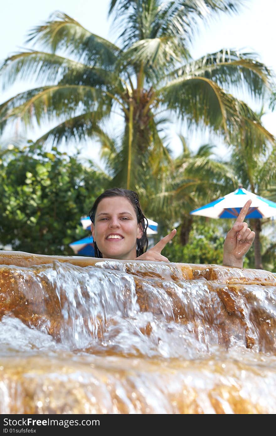 Young woman in a beautiful pool with palms in the background. She is pointing up. Young woman in a beautiful pool with palms in the background. She is pointing up.