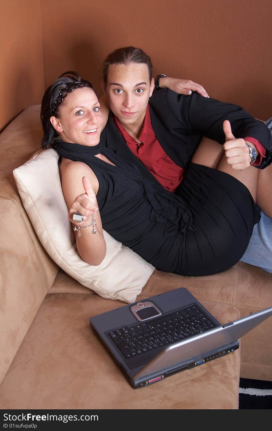 Young couple on the couch surfing the web with their laptop - showing a thumbs up sign. Young couple on the couch surfing the web with their laptop - showing a thumbs up sign.