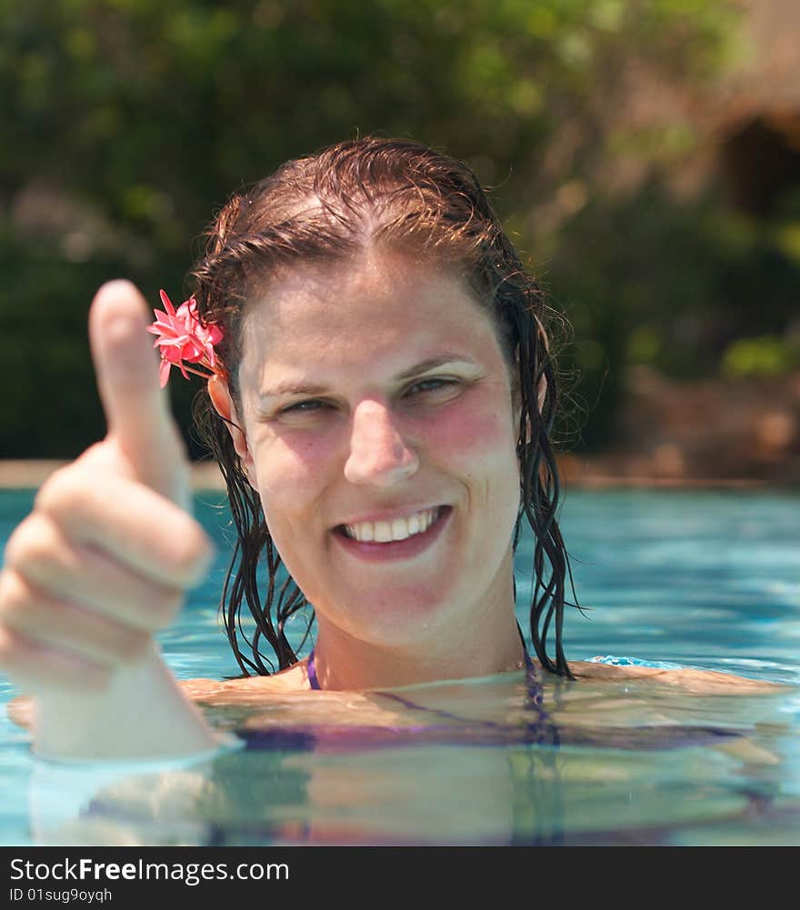 Young woman in a beautiful pool with palms in the background. She is showing a thumbs up sign. Young woman in a beautiful pool with palms in the background. She is showing a thumbs up sign.