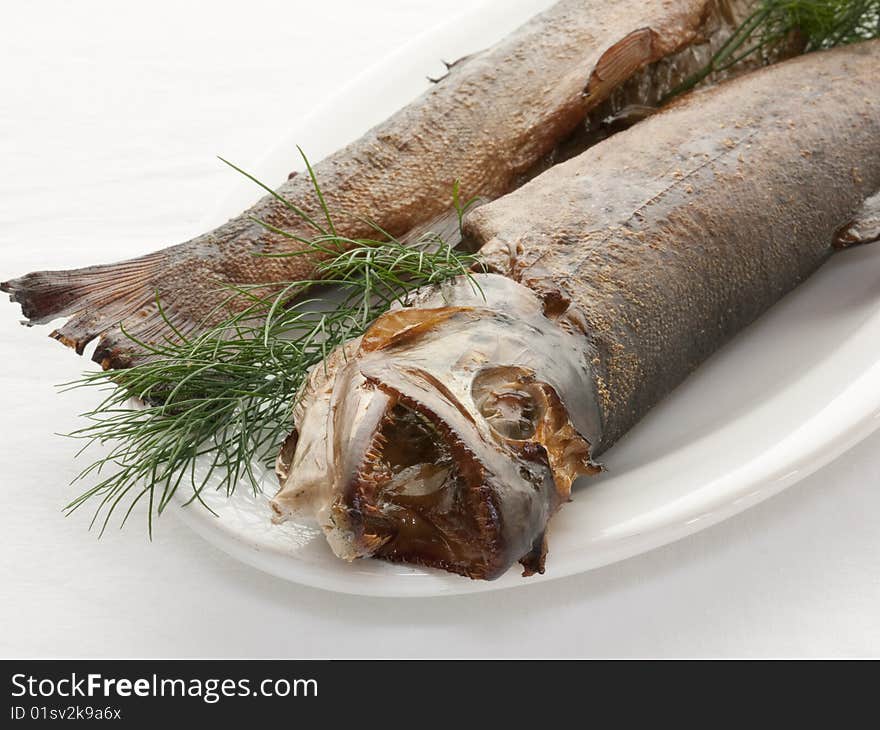 Two smoked trout on a white plate with a dill decoration