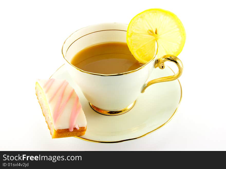 Tea in a cup and saucer with pink slice of cake and a slice of lemon on a white background. Tea in a cup and saucer with pink slice of cake and a slice of lemon on a white background