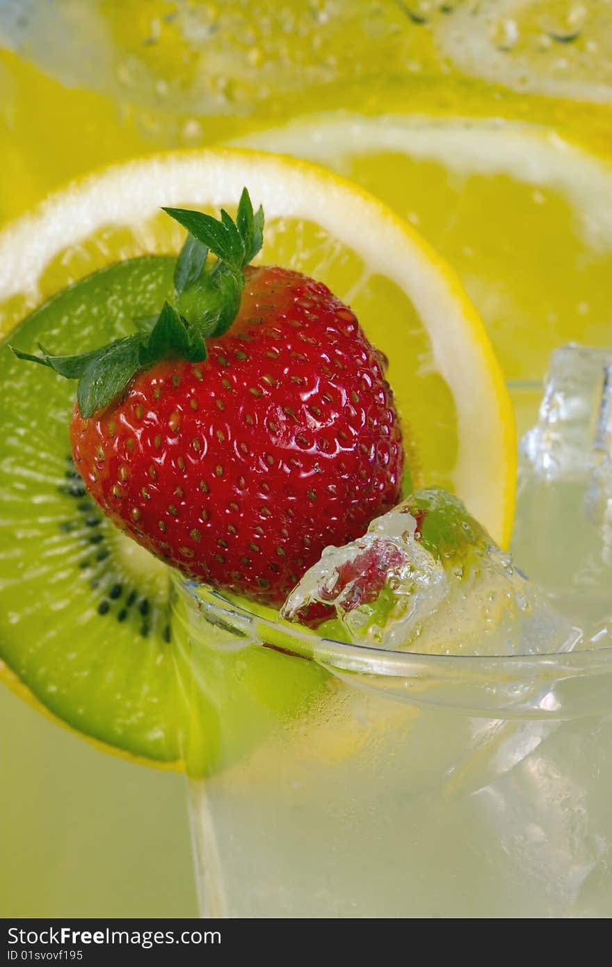 A luscious red strawberry on glass of iced lemonade with kiwi and lemon slice in background. A luscious red strawberry on glass of iced lemonade with kiwi and lemon slice in background