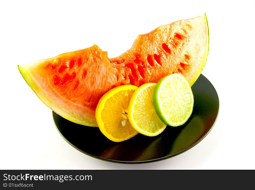 Slice of red juicy watermelon with a slice of lemon, lime and orange on a black plate with a white background. Slice of red juicy watermelon with a slice of lemon, lime and orange on a black plate with a white background