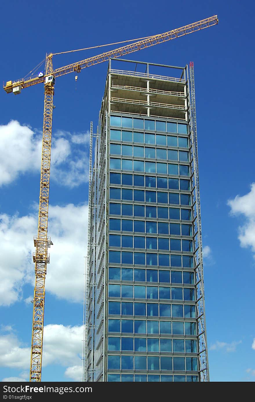 On a photo: Building and crane on a background of the blue sky.