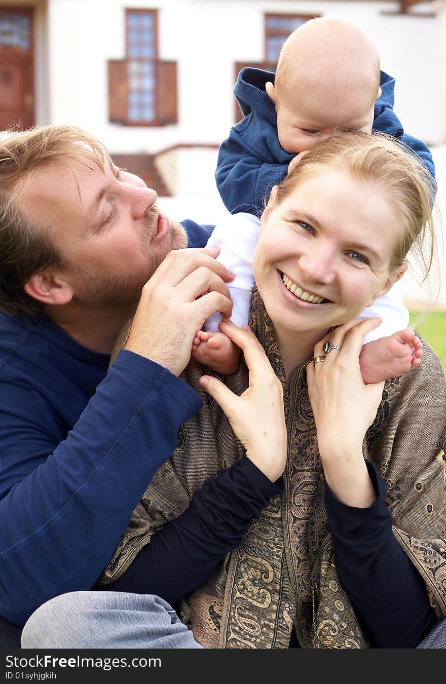 Beautiful happy family of three sitting on the grass laughing. Focus is on the mother. Beautiful happy family of three sitting on the grass laughing. Focus is on the mother