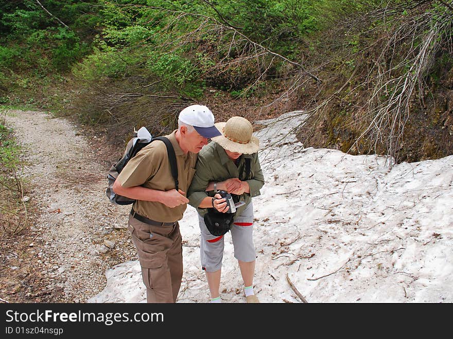 Summer day. The Alpes. Road to wood. Along road trees are tumbled down. On road – not thawn snow. These are the rests of a spring avalanche. The woman and the man get on a dense snow hill. Summer day. The Alpes. Road to wood. Along road trees are tumbled down. On road – not thawn snow. These are the rests of a spring avalanche. The woman and the man get on a dense snow hill.