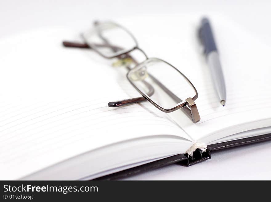 The black opened notebook with blank pages, with the handle laying on it and glasses. The black opened notebook with blank pages, with the handle laying on it and glasses