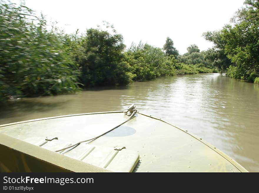 Baw of the motor boat sails down the river. The trees on the left part of the foto are blurred. Focus is under the boat's baw