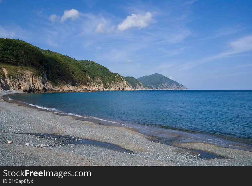 A landscape on Japanese sea. A beach with grey pebbles< green capes and cloudy sky. A landscape on Japanese sea. A beach with grey pebbles< green capes and cloudy sky.