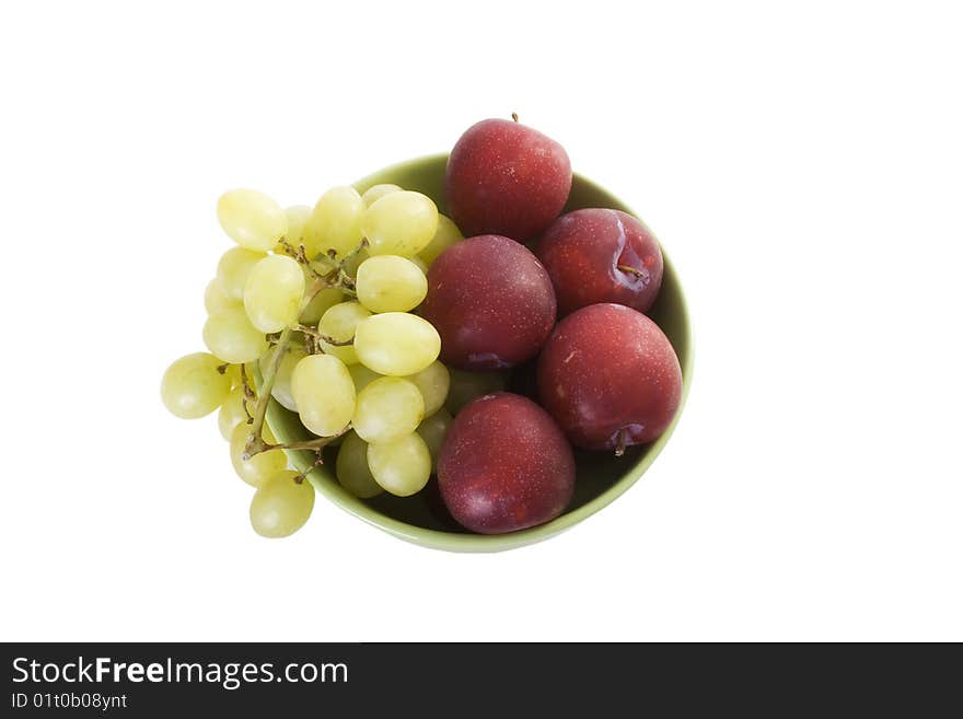 Green bowl with red plums and green grapes on white table. Green bowl with red plums and green grapes on white table.