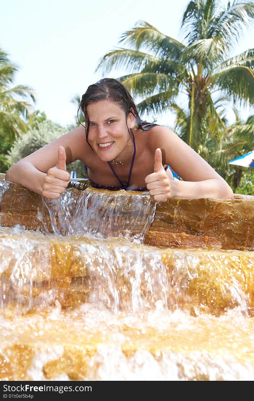 Young woman in a beautiful pool with palms in the background. She is showing a thumbs up sign. Young woman in a beautiful pool with palms in the background. She is showing a thumbs up sign.