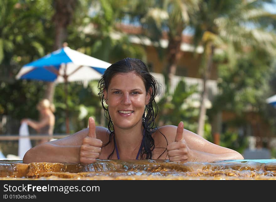 Young woman in a beautiful pool with palms in the background. She is showing a thumbs up sign. Young woman in a beautiful pool with palms in the background. She is showing a thumbs up sign.