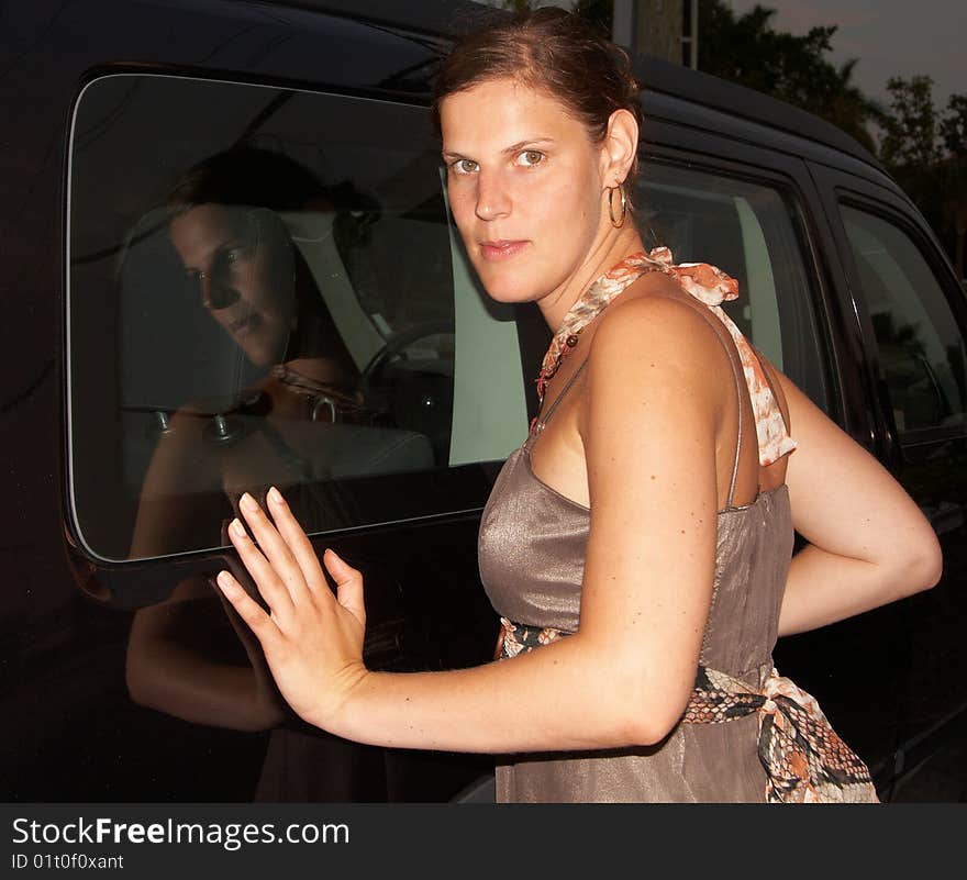 Young woman posing in front of a black SUV. Her body is mirrored in the car. Young woman posing in front of a black SUV. Her body is mirrored in the car.