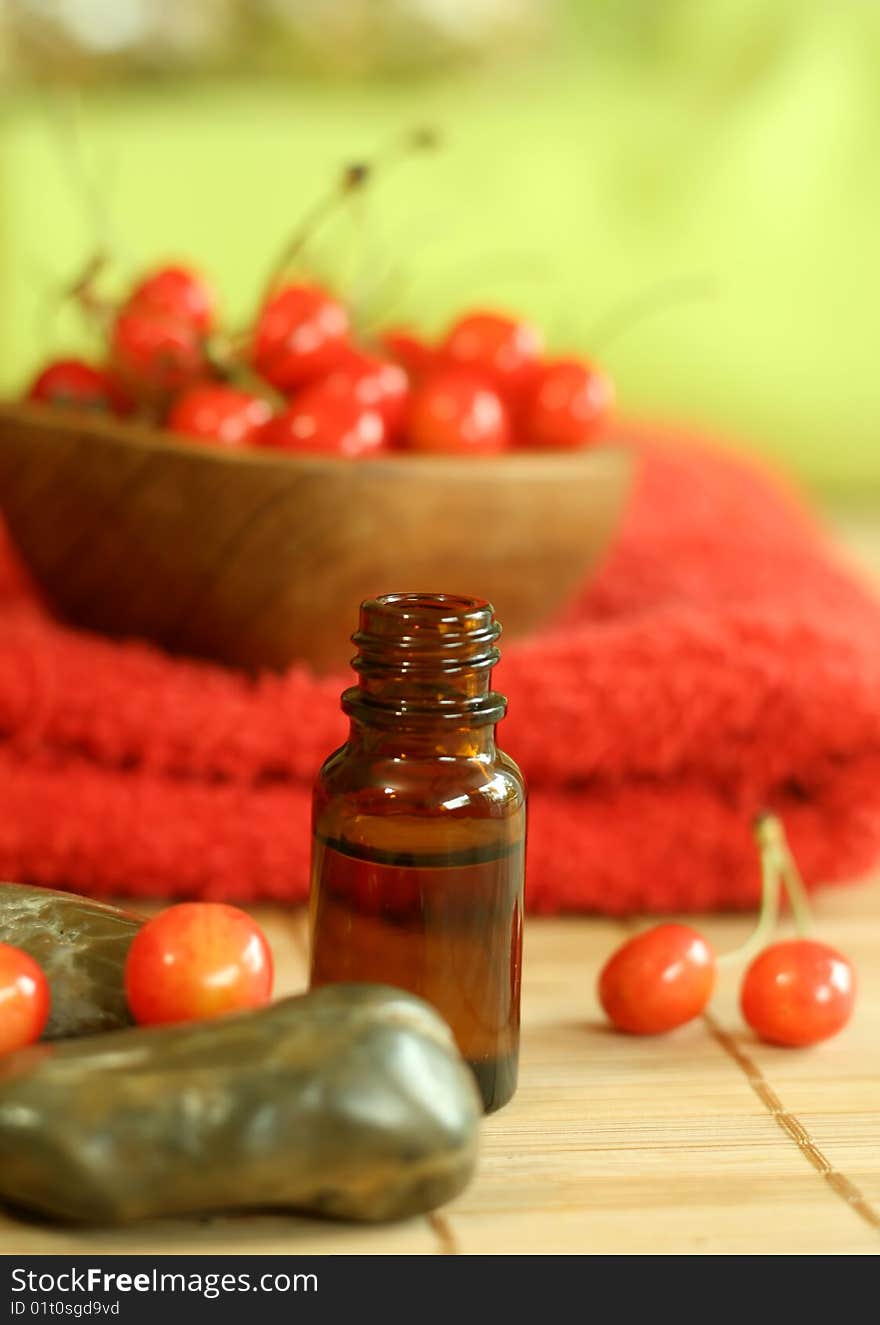 bottle of essence oil, stone, fresh cherry and red towel