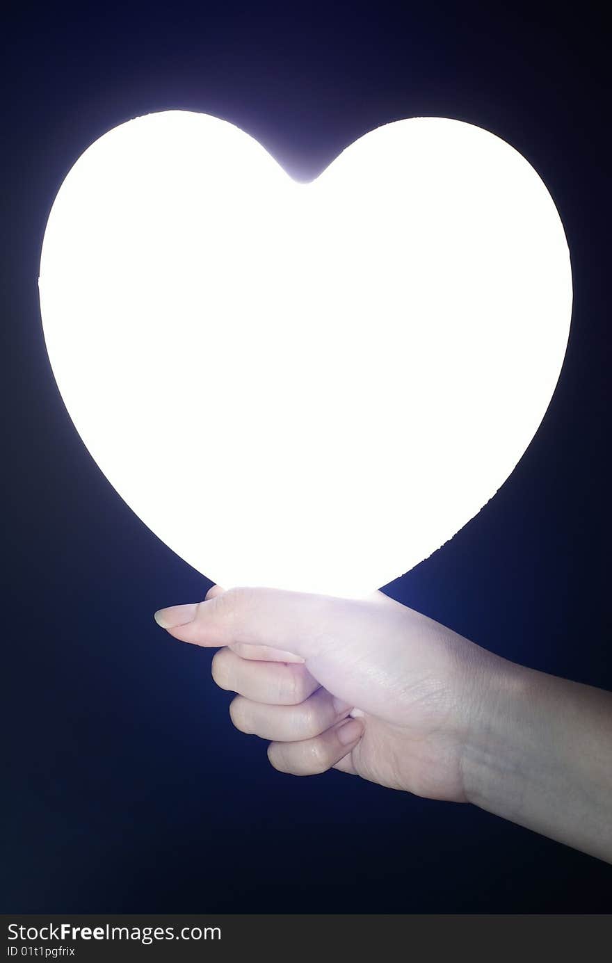 Bright heart in female hand with black background