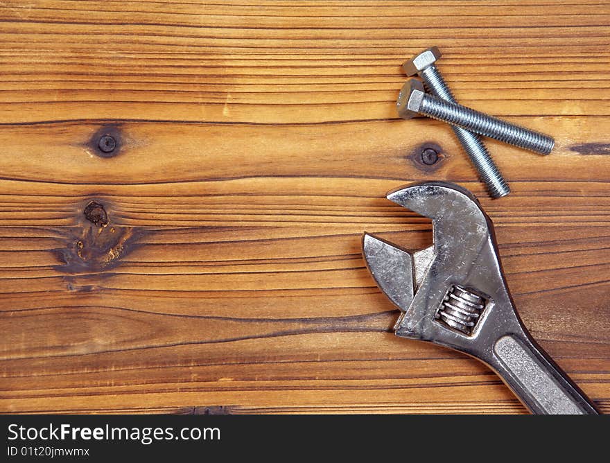 Screws and spanner on wood board.