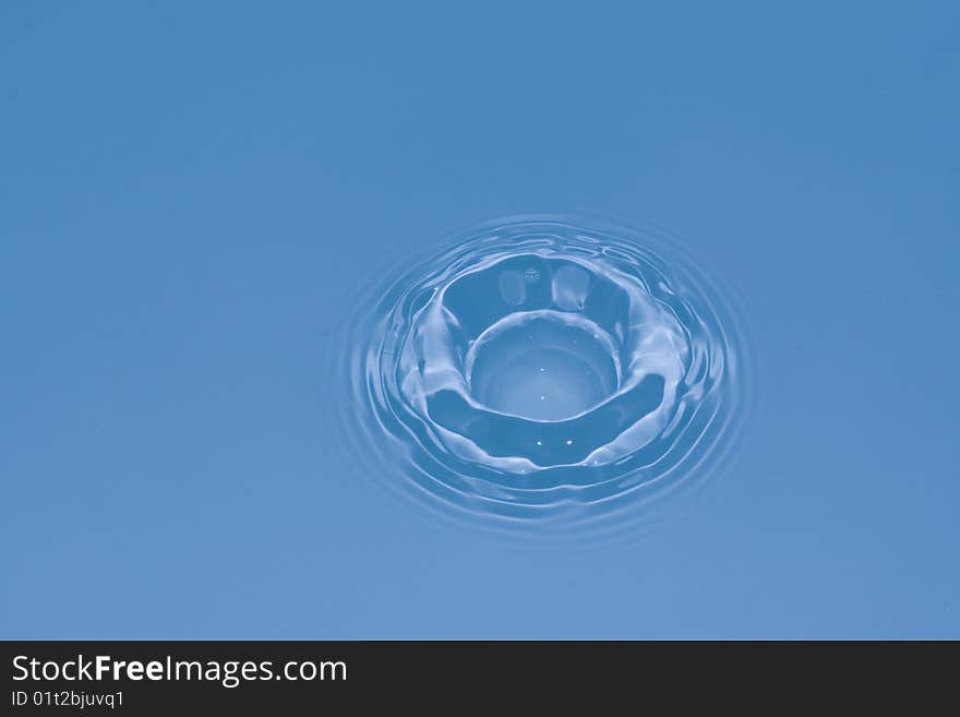 Water drop falling in water and creating a dip and ripples. Water drop falling in water and creating a dip and ripples