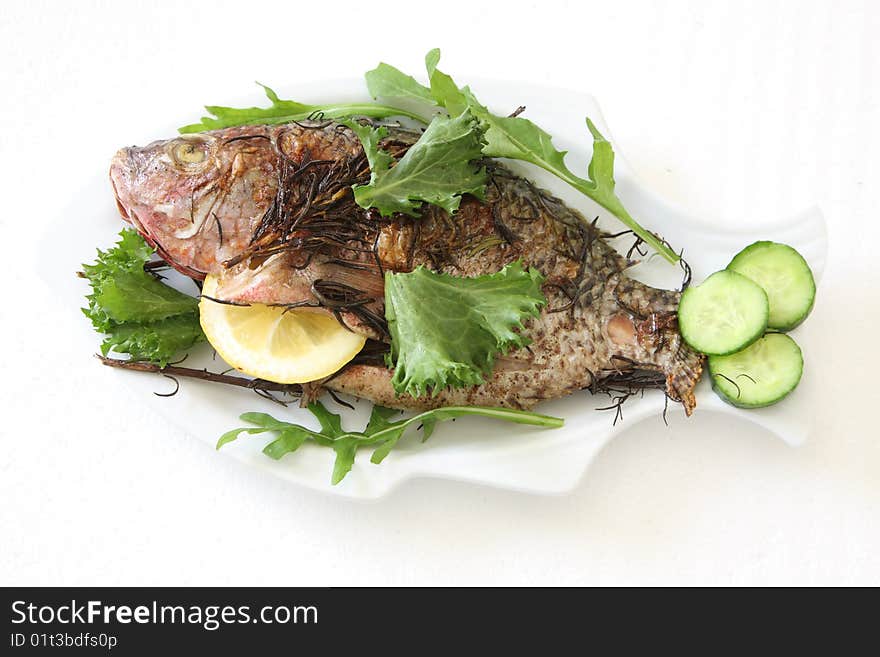 Grilled fish with greens lemon and cucumber on the plate over white